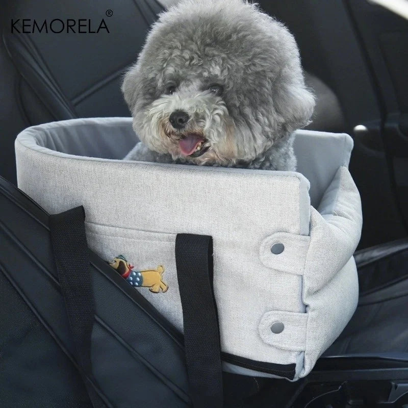 Dog in a gray pet seat carrier with KEMORELA branding inside a car.